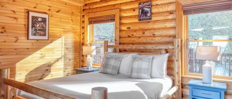 A wooden cabin bedroom with a bed, a nightstand, a lamp, and a framed picture on the wall.
