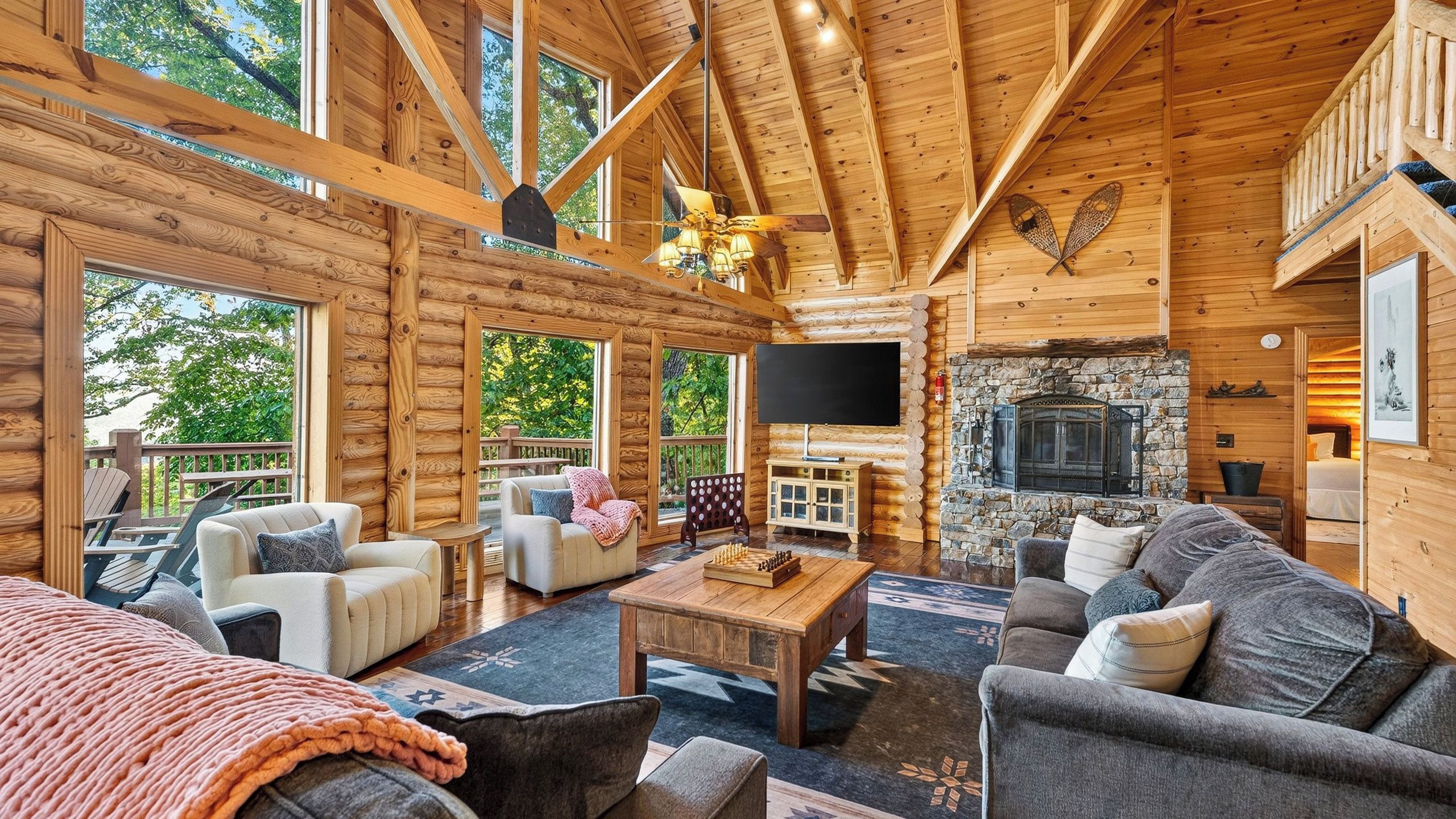 A log cabin interior with a fireplace, wooden furniture, and large windows.