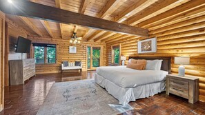 A log cabin bedroom with a bed, bedside table, dresser, and a television.