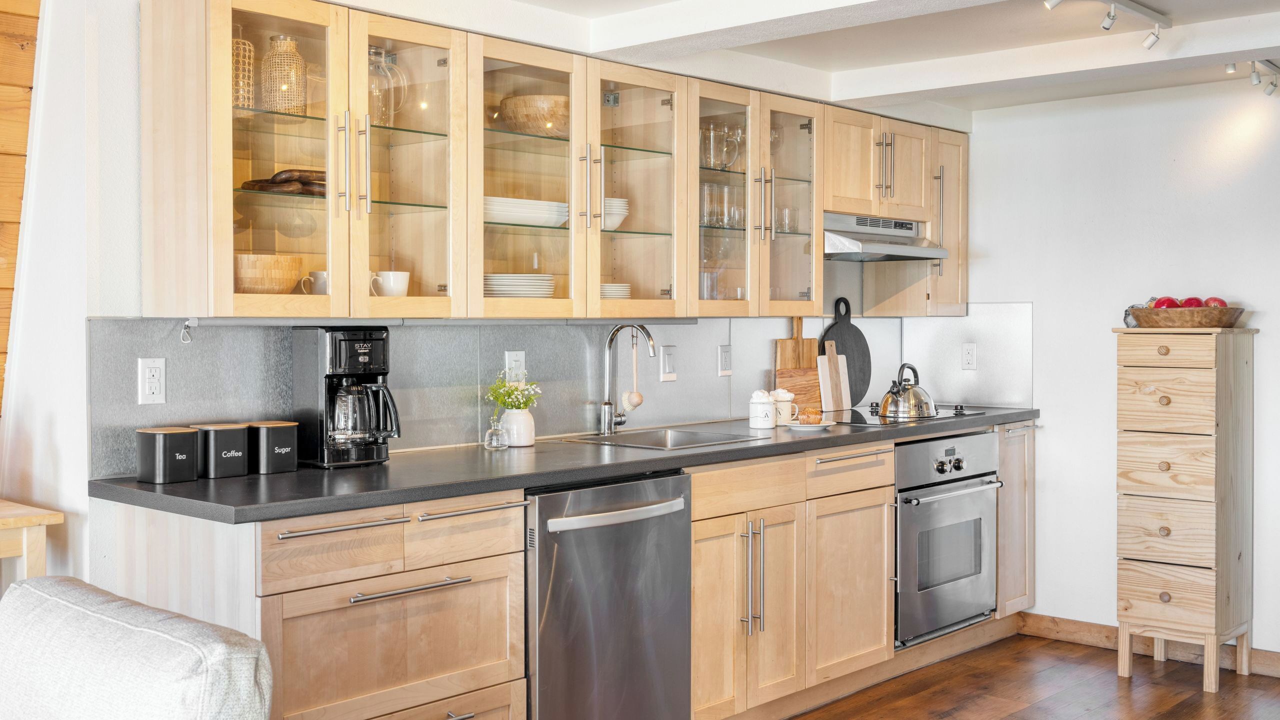 A modern kitchen with wooden cabinets, a stainless steel dishwasher, and a built-in oven.