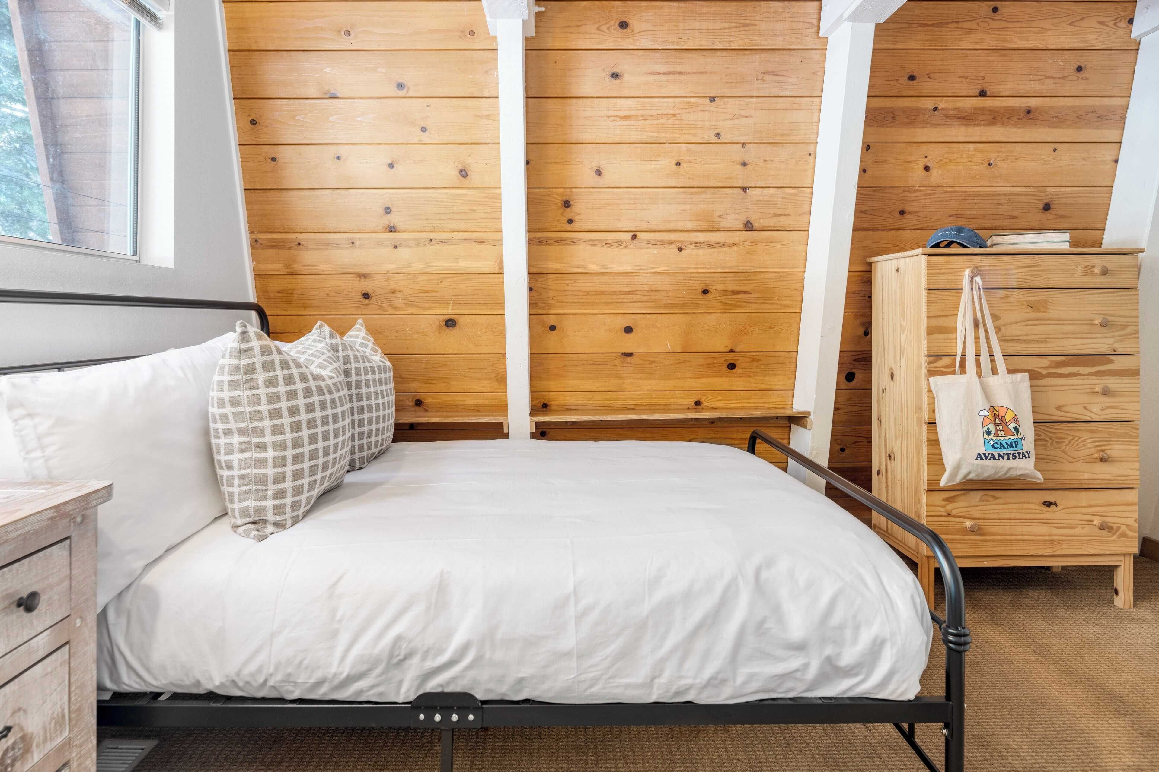 A bedroom with a wooden ceiling, a bed with white bedding, a wooden dresser, and a window.