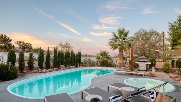 A swimming pool with lounge chairs and a hot tub, surrounded by palm trees and a fence. - Archie by Avantstay Desert Retreat w/ Pool, Edge of Joshua Tree, Bonus Casita for Group Travel (Yucca Valley)