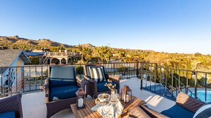 A terrace with wicker furniture, a pool, and a view of a hilly landscape. - Archie by Avantstay Desert Retreat w/ Pool, Edge of Joshua Tree, Bonus Casita for Group Travel (Yucca Valley)