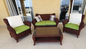 A wicker sofa set with green cushions and a glass coffee table in a sunlit room with a view through large windows. - Pathos Penthouse A Slice of Paradise (Geroskipou)