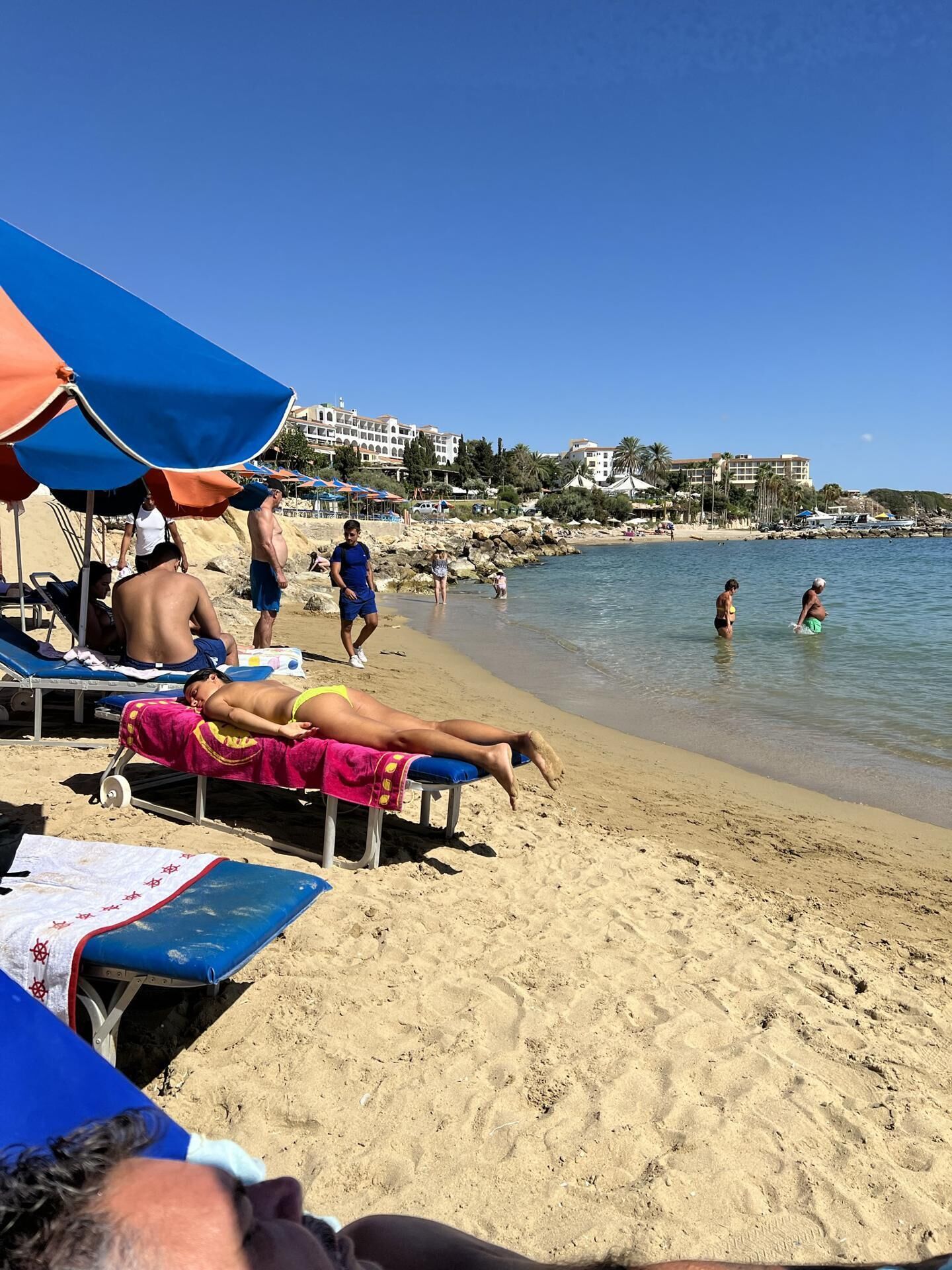 Una playa con tumbonas, sombrillas y un cielo azul despejado.
