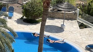 A swimming pool with two people sunbathing, surrounded by palm trees and lounge chairs. - Pathos Penthouse A Slice of Paradise (Geroskipou)