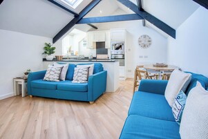 Eine moderne Loftwohnung mit blauem Sofa, Holzböden, einer Küche mit weißen Schränken und einem Dachfenster.