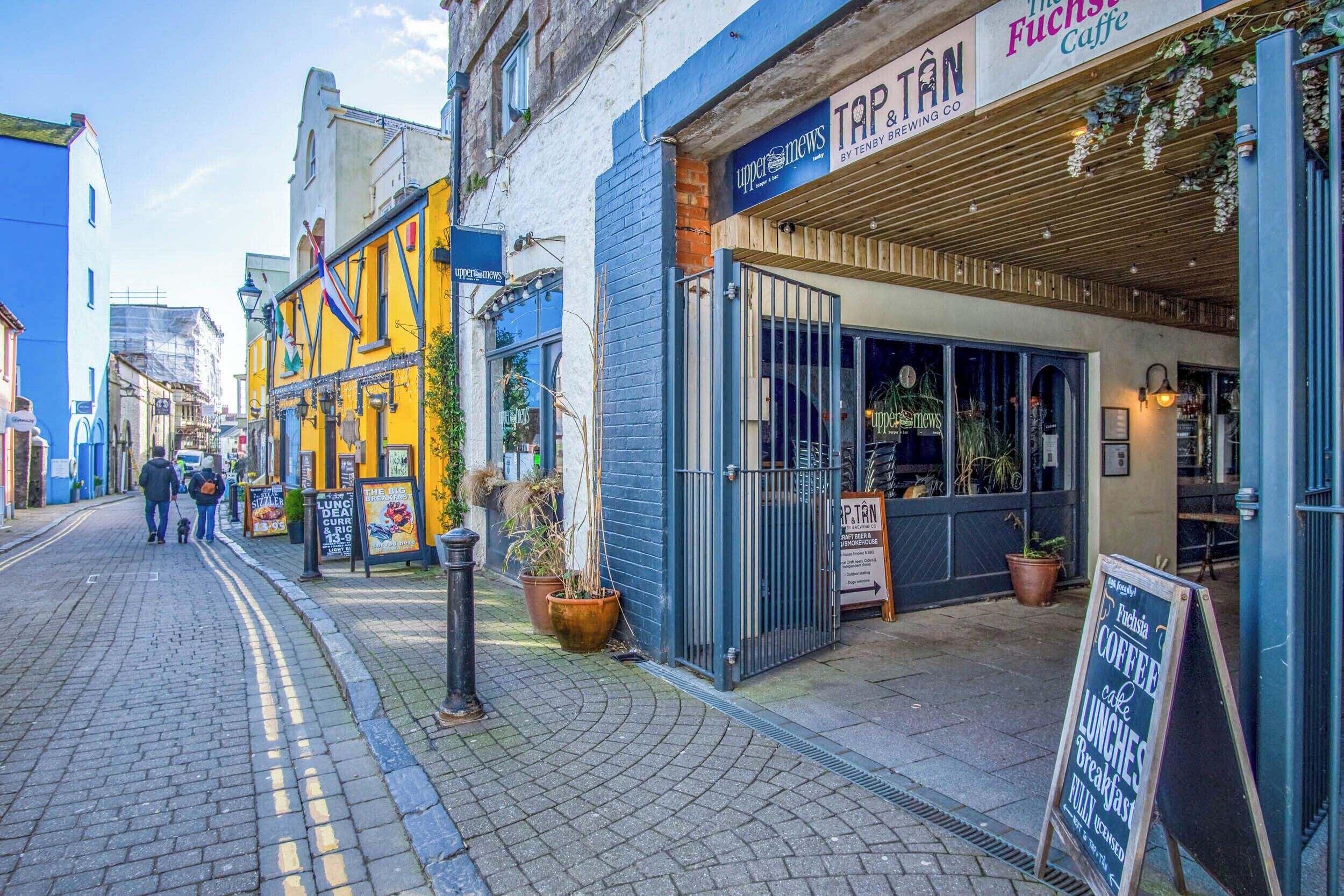 Eine Straße mit einem Café namens "Tap & Tan" und einem Schild, das "The Fuchsia Caffe" bewirbt.