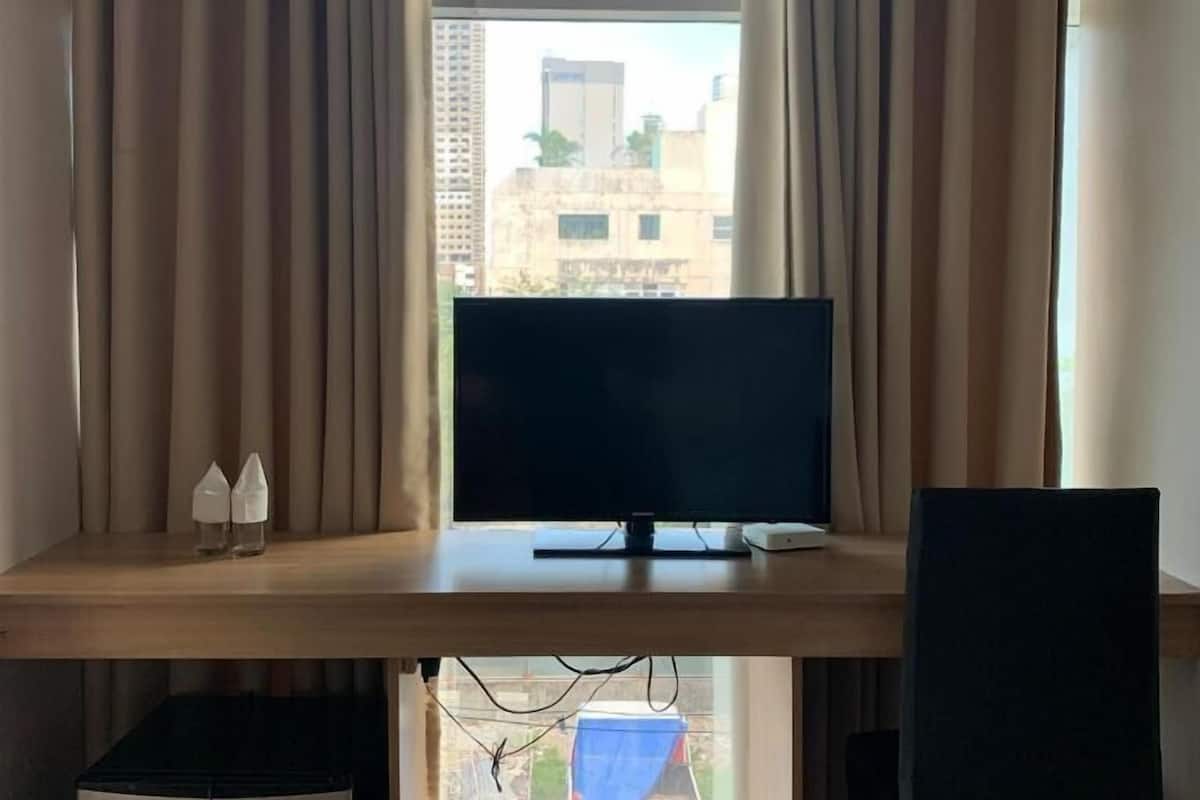 Une pièce comprenant un bureau, un écran d’ordinateur et une fenêtre avec des rideaux.