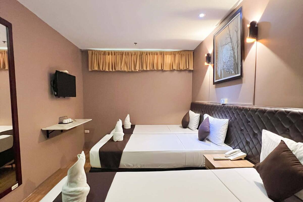 Une chambre d’hôtel avec deux lits, un téléviseur à écran plat, un tableau au mur et une petite étagère.