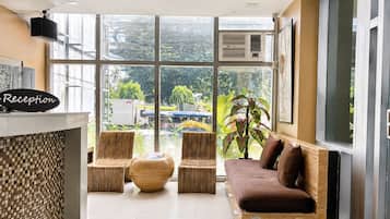 A reception area with a reception desk, wicker furniture, a brown sofa, and large windows with a view of the outside.