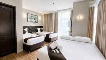 A hotel room with two beds, a large window with curtains, a flat-screen TV, and a dark wooden door.