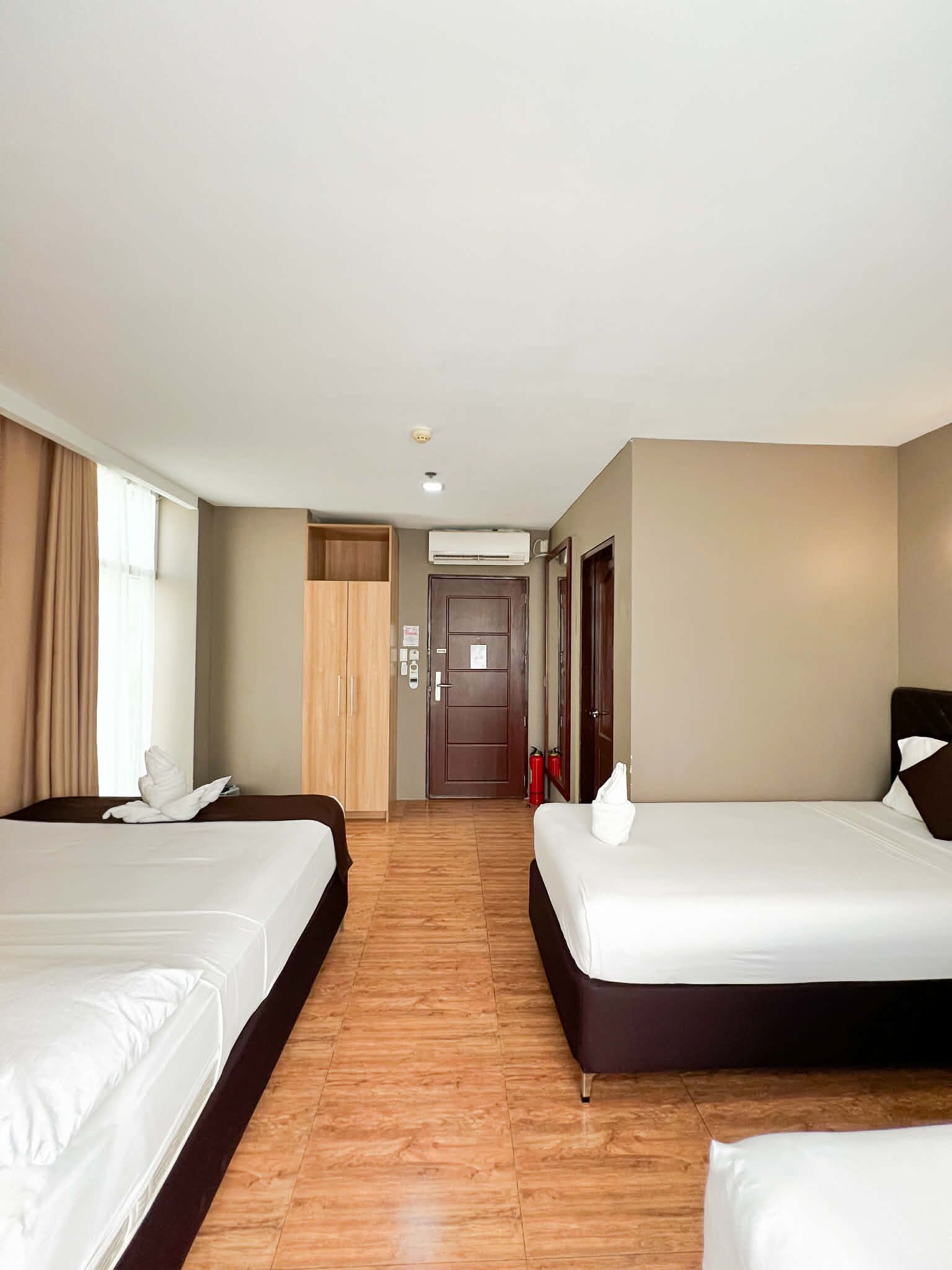 A hotel room with two beds, a wooden wardrobe, a door, and an air conditioning unit.