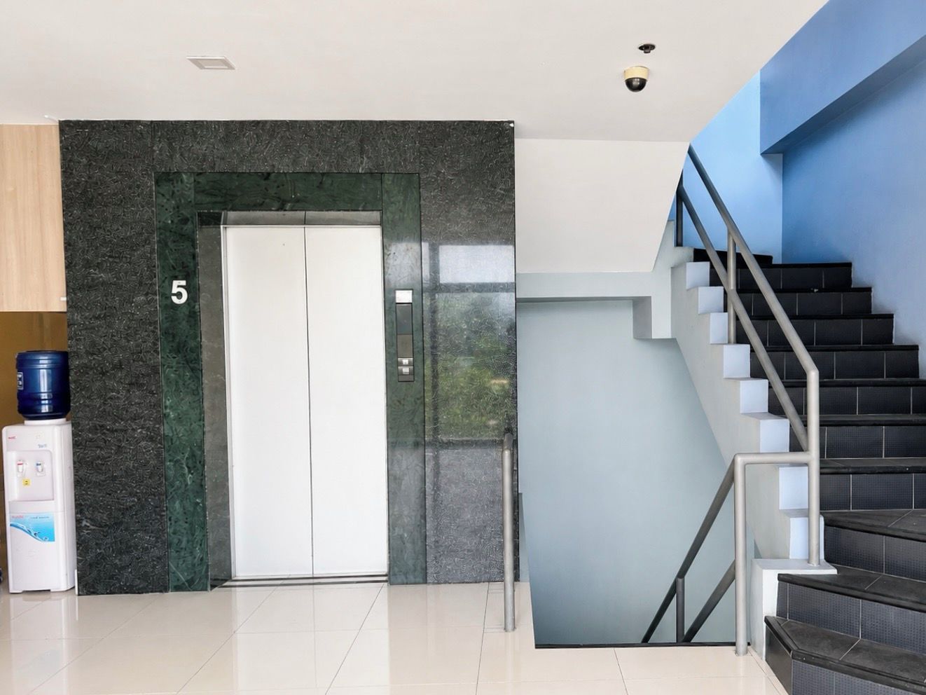 A modern interior with a water dispenser, a double door elevator, and a staircase.
