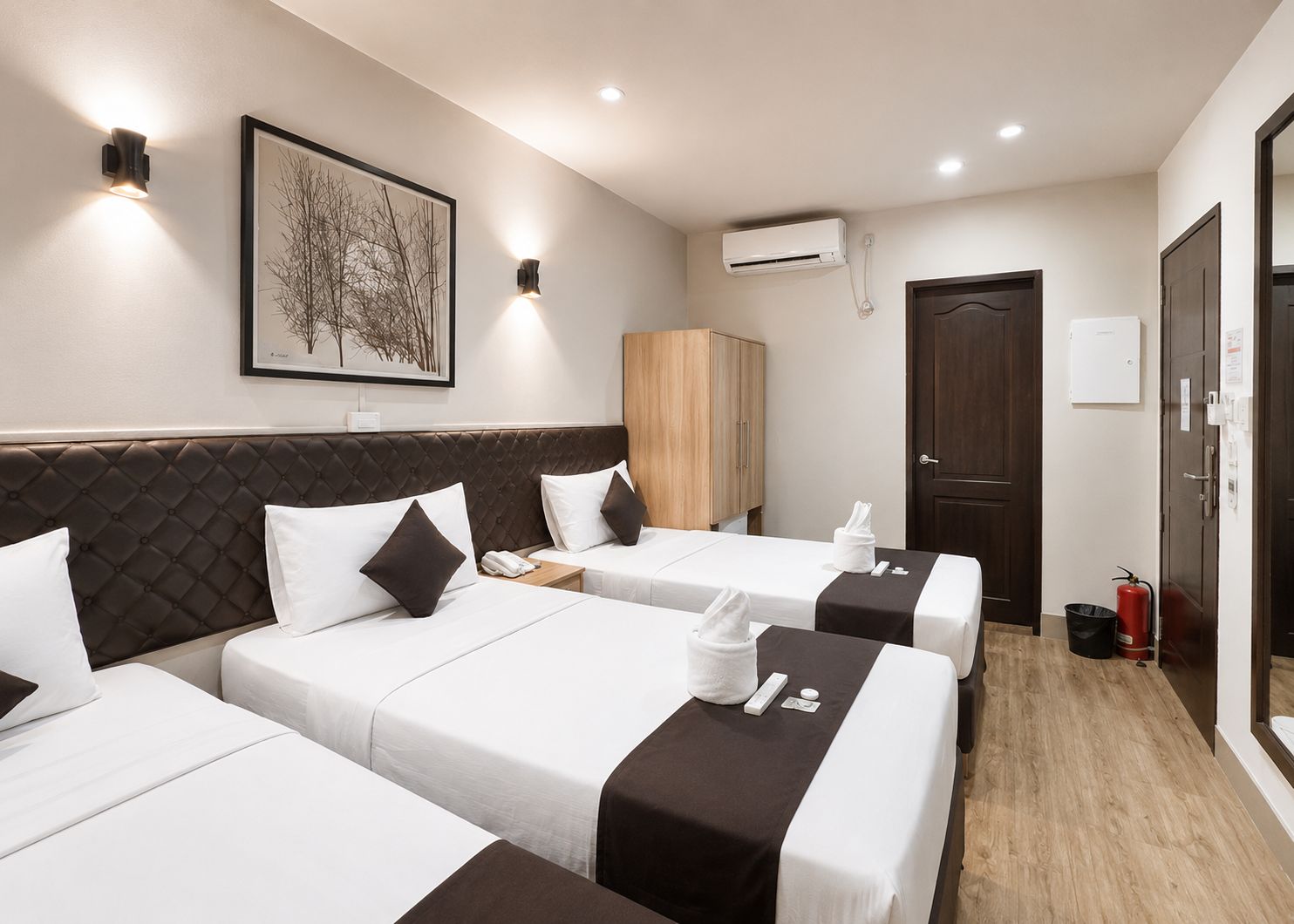 Habitación de hotel con tres camas, un armario, un equipo de aire acondicionado y un cuadro en la pared.