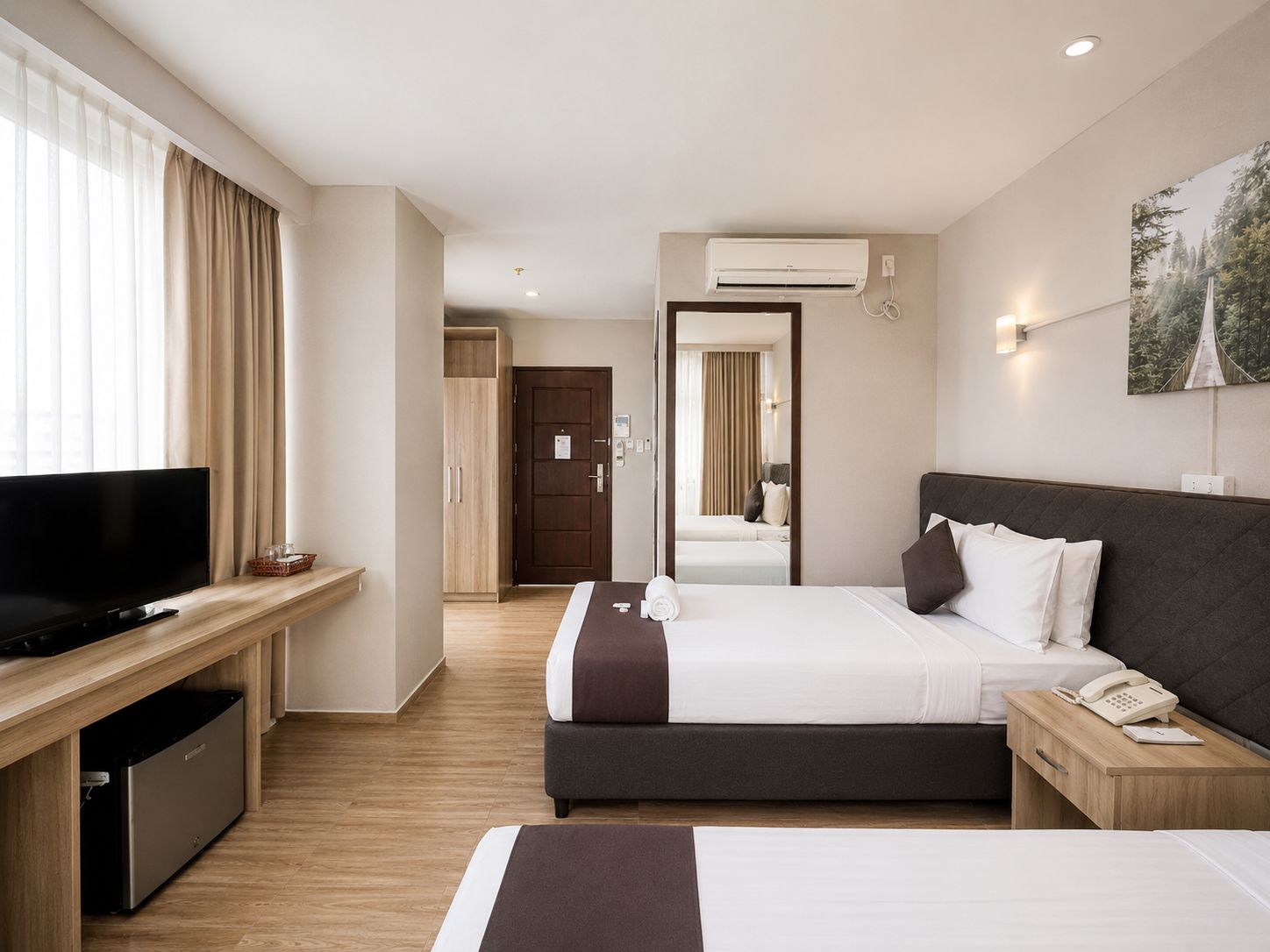 Een hotelkamer met een televisie, een bureau, een bed, een nachtkastje met telefoon, en een groot raam met gordijnen.