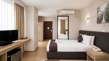 Habitación de hotel con televisor, escritorio, cama, mesita de noche con teléfono y un amplio ventanal con cortinas.