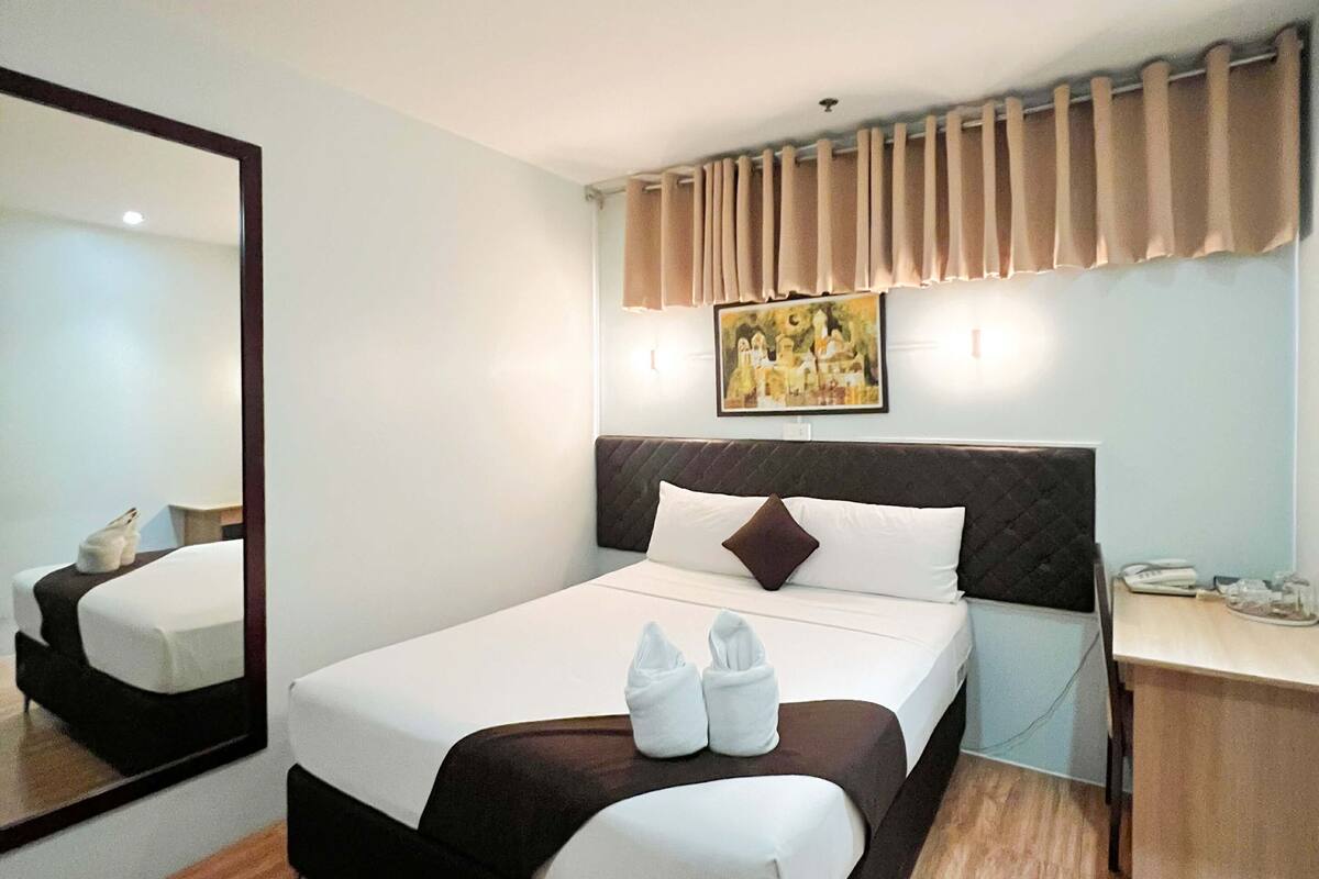 Une chambre d’hôtel avec un lit, un bureau, une chaise, un miroir et un tableau au mur.