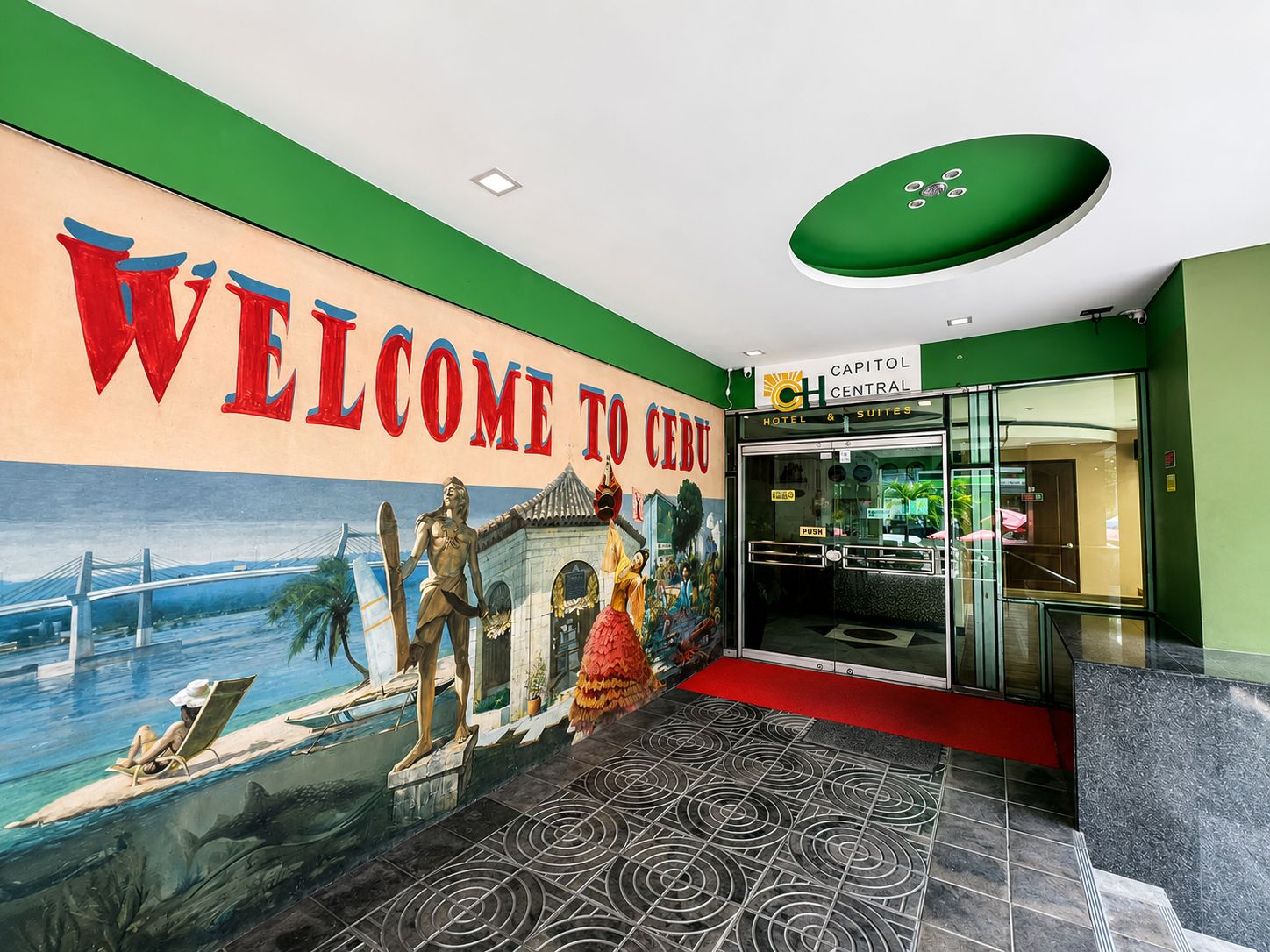 A hotel lobby with a mural, a reception desk, and a glass entrance.