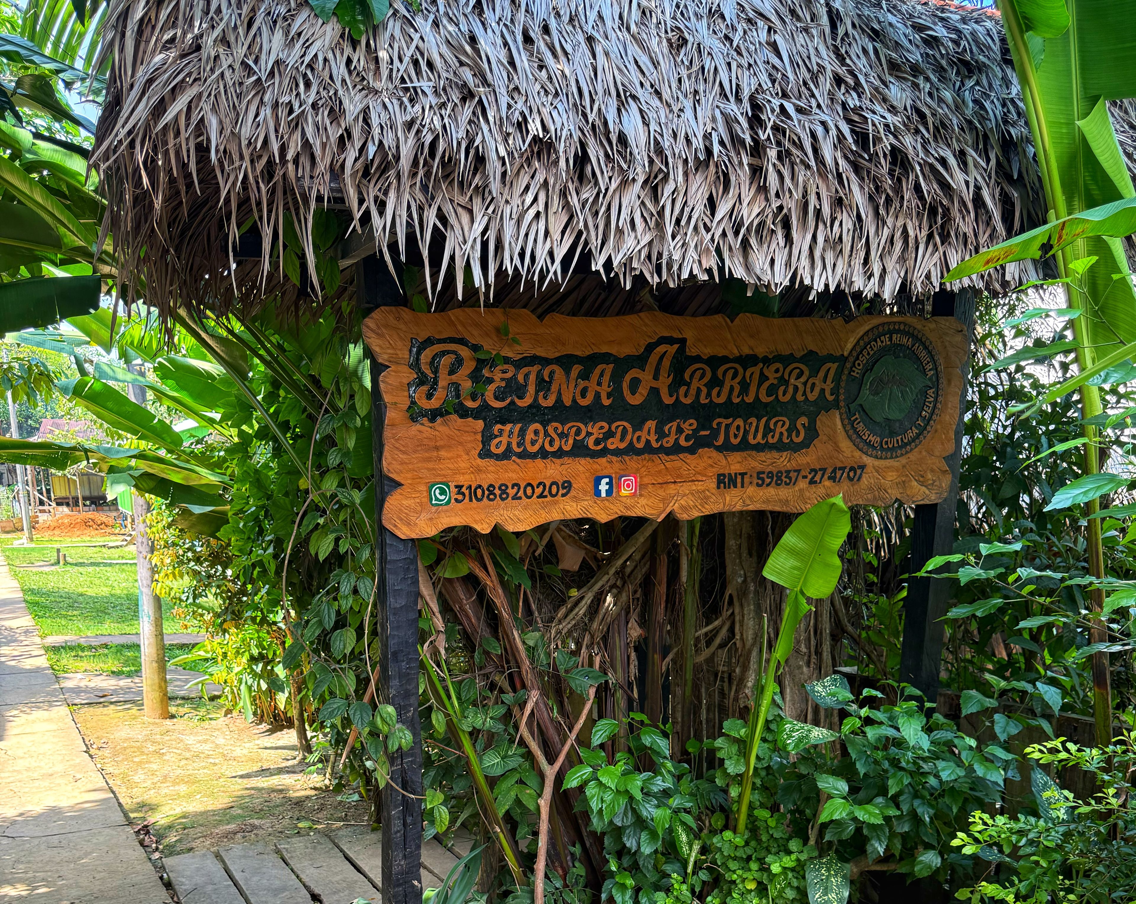 A wooden sign with the text 'REINA ARRERA HOSPEDADE-TOURS' and a contact number.