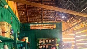 A rustic kitchen with wooden shelves, a table with a floral tablecloth, and a thatched roof. - Authentic Amazon | Indigenous Lodging and Jungle Tours (Loreto Mocagua)
