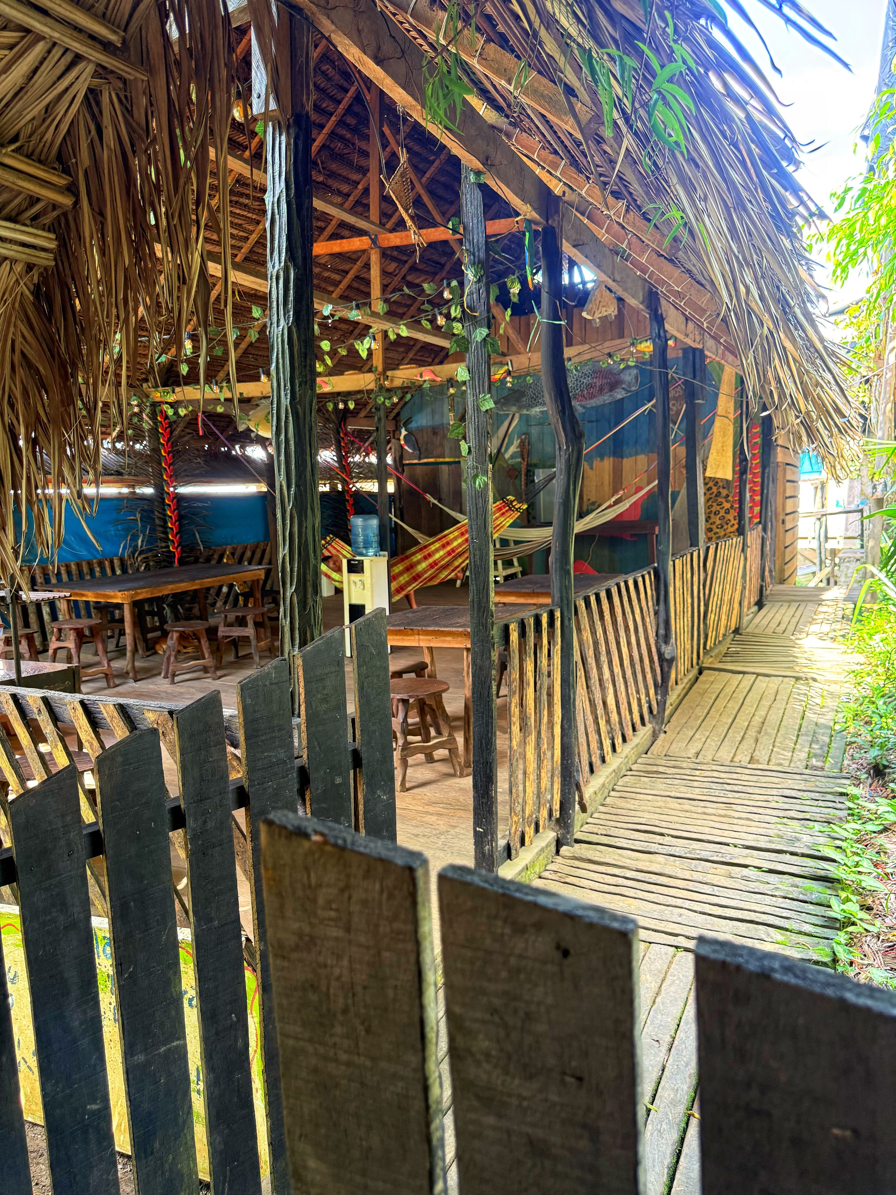 A wooden deck with a thatched roof structure, wooden benches, and a hammock.