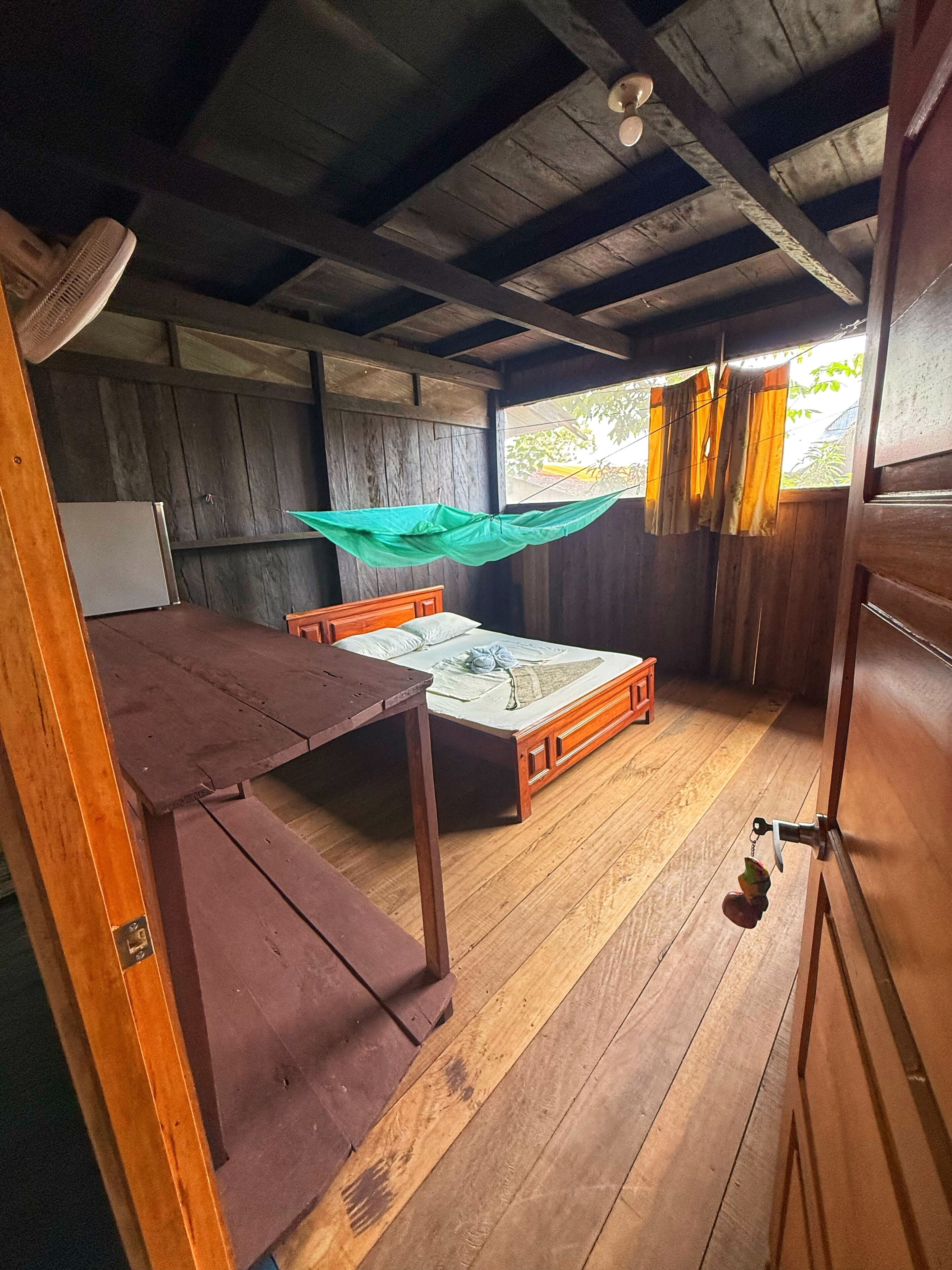 A wooden interior with a bed, a table, and a ceiling fan.