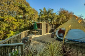 A wooden deck with a small outdoor seating area, a thatched-roof tent, and a wooden cabin. - Te Tiro Accommodation (Waitomo Caves)