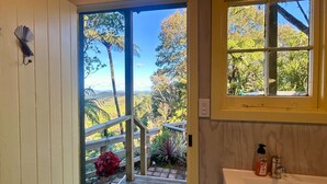 A bathroom with a large window, a wooden deck with a railing, and a view of the outdoors. - Te Tiro Accommodation (Waitomo Caves)