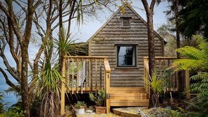 A wooden cabin with a small porch, surrounded by dense vegetation and trees. - Te Tiro Accommodation (Waitomo Caves)