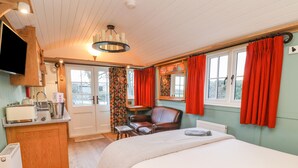 A bedroom with a bed, a chair, a desk with a kettle, a radiator, and a TV mounted on the wall. - Arts and Crafts (York)