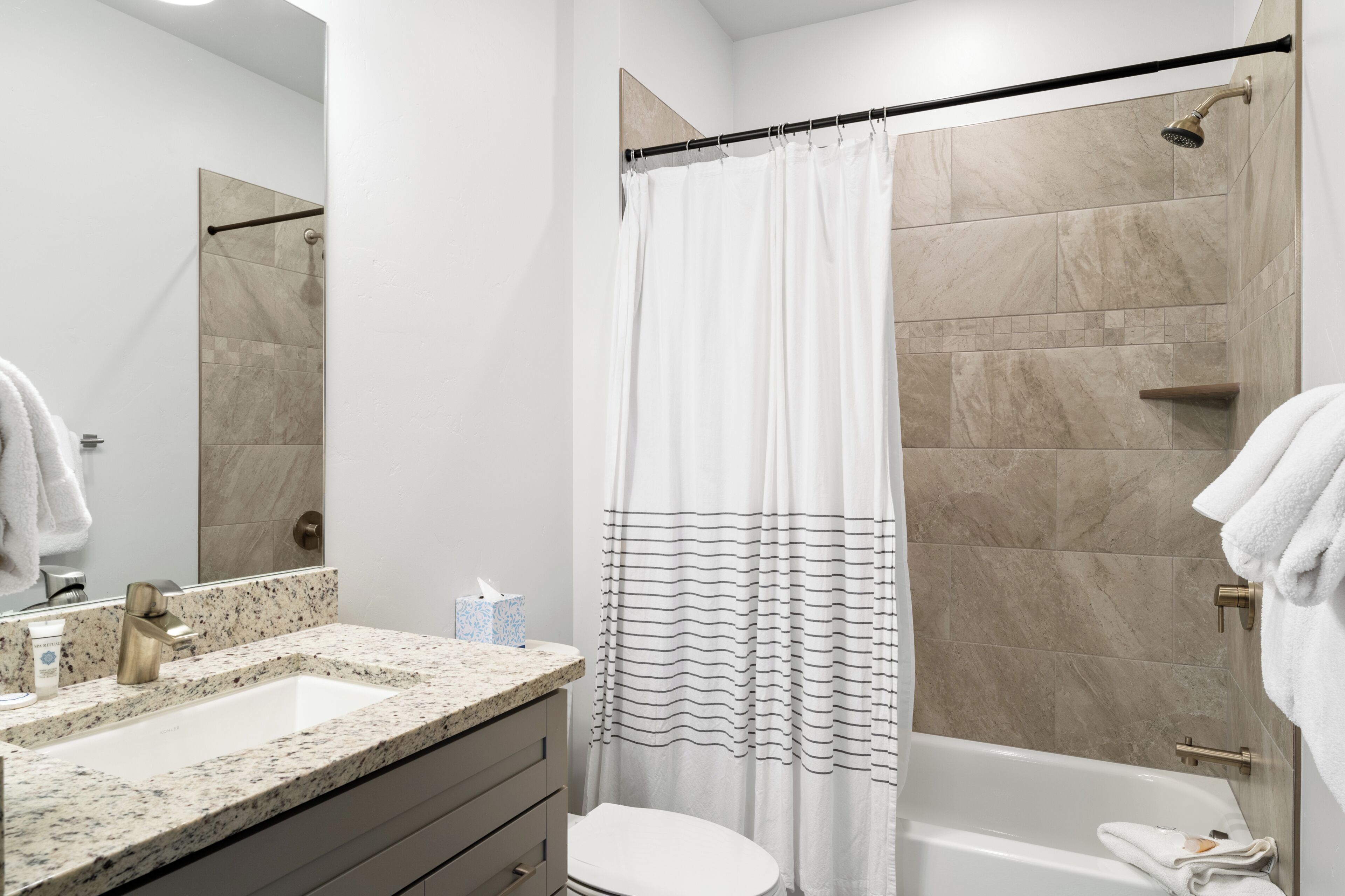 A modern bathroom with a freestanding bathtub, a shower curtain, a sink with a marble countertop, and a toilet.