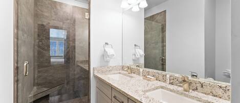 Un baño moderno con cabina de ducha, un espejo grande y encimera de granito.