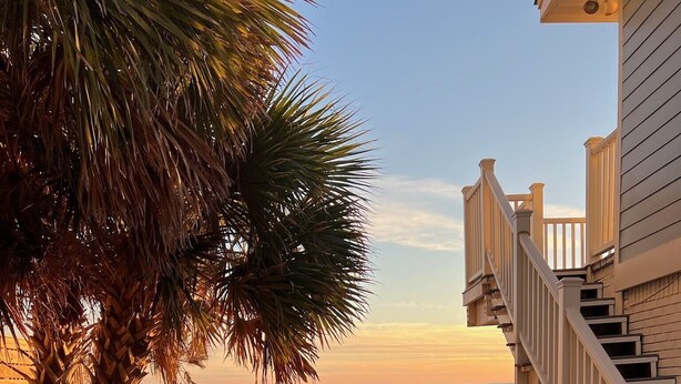 Ein hölzerner Steg führt zu einem Strand, am rechten Rand befindet sich eine Holztreppe.