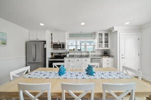 A modern kitchen with white cabinets, a stainless steel refrigerator, a microwave, and a sink. There is a dining table with chairs and a sign above the window that reads "FLIP FLOP LIFE". - 🌊 Cyan Wave | West End Panama City Beach / 30A | Pool / Beach Access |Sleeps 12 (Panama City Beach)