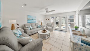 Ein geräumiges Wohnzimmer mit grauem Sofagarnitur, einem Couchtisch und einem Deckenventilator.