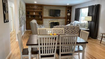 Un salon avec une cheminée, un téléviseur, une table à manger avec des chaises et un canapé.