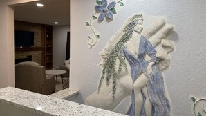 A wall mural of a woman in a blue dress with a flower and leaves, a stone fireplace, a television, and a seating area with a chair and a small table.