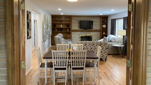 A cozy living room with a dining area, wooden flooring, a fireplace, and a television.