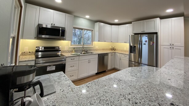A modern kitchen with white cabinets, stainless steel appliances, granite countertops, and a window providing natural light.
