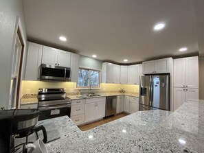 A modern kitchen with white cabinets, stainless steel appliances, granite countertops, and a window providing natural light.