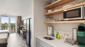 A modern kitchen with a microwave, coffee maker, and a sink. There are wooden shelves above the counter and a balcony with a view of the city. - Bayside Sandestin studio @ Links golf & conference center (Miramar Beach)