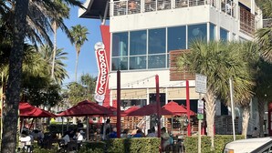 A modern building with a balcony, surrounded by palm trees and outdoor seating. - Clearwater Beach, Your Dream Vacation, Condo (Clearwater)