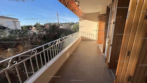 Un balcon doté d’une rambarde en métal, d’un sol carrelé et offrant une vue sur les environs, notamment sur les arbres et un bâtiment.