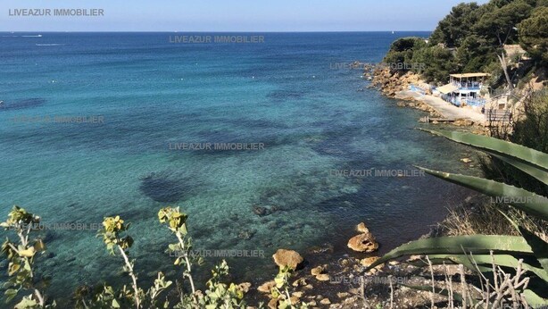 Une vue côtière avec une eau turquoise cristalline, une côte rocheuse et un petit bâtiment, une plage se trouvant à l’arrière-plan.