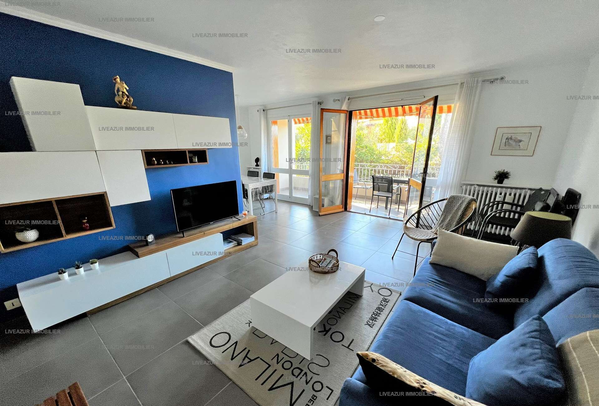 A modern living room with a blue accent wall, a flat-screen TV, a sofa, and a dining area with a table and chairs.