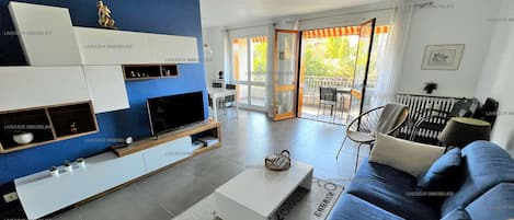 A modern living room with a blue accent wall, a flat-screen TV, a sofa, and a dining area with a table and chairs.