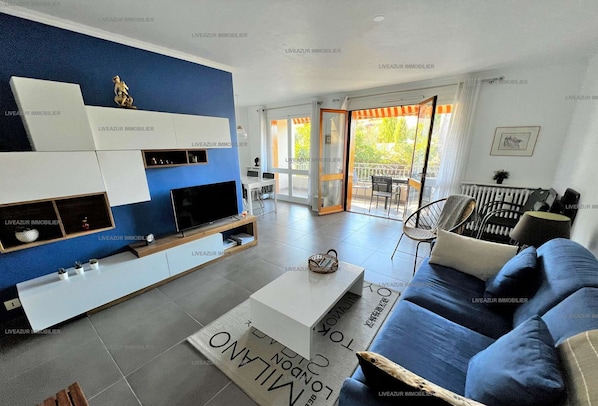 Un salon moderne avec un mur d’accent bleu, un téléviseur à écran plat, un canapé et un coin repas comprenant une table et des chaises.