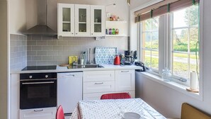 Cocina compacta con armarios blancos, salpicadero de azulejos y ventana con vista a vegetación.