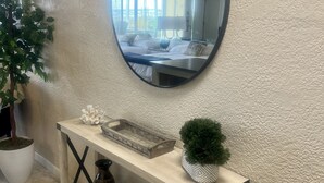 A wooden console table with a mirror above it, a small potted plant, and a wicker basket with towels.